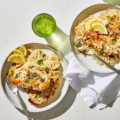 two plates of pasta with chicken and lemon wedges on the side next to a glass of green juice