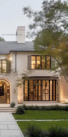 a large white house with lots of windows and lights on the front door is lit up at night