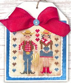 a cross stitch ornament with a red bow hanging from it's side