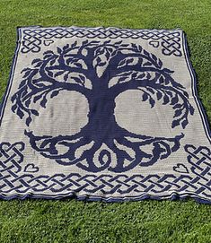 a blue and white tree of life rug sitting on top of a grass covered field