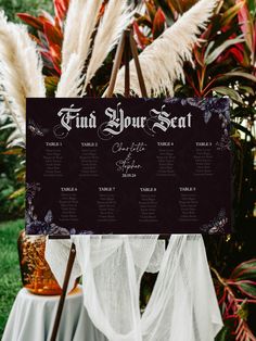 a black and white wedding seating chart on a wooden easel in front of some plants