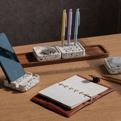 a wooden table topped with notebooks, pens and an open cell phone on top of it