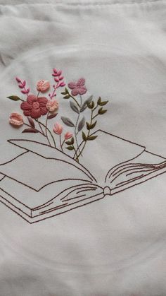 an open book with flowers on it is embroidered onto the side of a white shirt