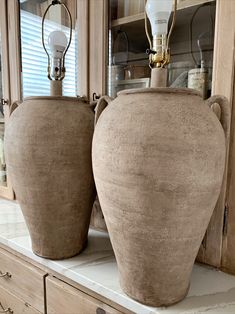 two large vases sitting on top of a counter in front of a mirror with light bulbs