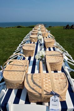 a long table with wicker baskets and flowers on it in front of the ocean