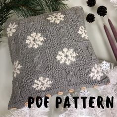 a gray knitted pillow sitting on top of a white christmas tree next to pine cones