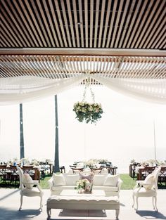 an outdoor seating area with white furniture and flowers hanging from the ceiling