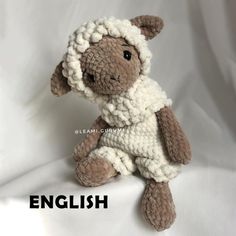 a small stuffed sheep is sitting on a white sheet and wearing a knitted outfit