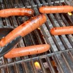 several hot dogs being grilled on a grill with tongs sticking out of them