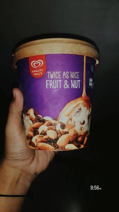 a hand holding up a cup of fruit and nut ice cream