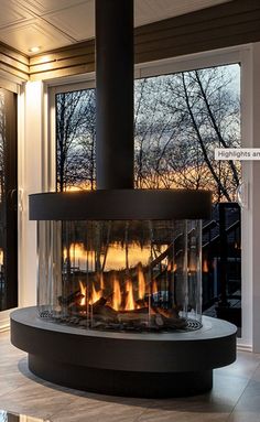 a modern fireplace in the middle of a living room with large windows overlooking trees and snow