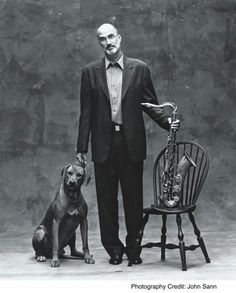 a man standing next to a dog in front of a chair with a saxophone on it