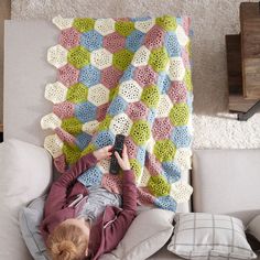 a woman laying on top of a couch next to a crocheted blanket holding a cell phone