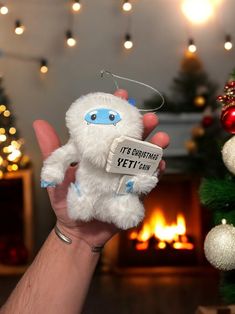 a hand holding a white stuffed animal in front of a christmas tree