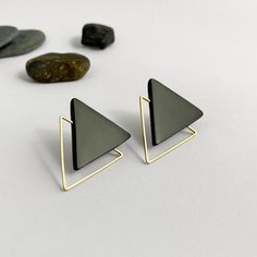 two triangle shaped earrings sitting on top of each other next to some rocks and stones