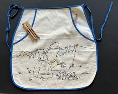 an embroidered apron with blue trim and two wooden utensils