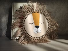 a lion head made out of hay with eyes closed and ears curled up, sitting on a shelf next to a book