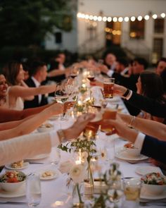 a group of people sitting at a long table toasting with wine glasses