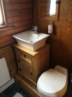 a white toilet sitting next to a sink in a bathroom under a wooden window sill