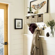 a coat and hat are hanging on the wall next to a shelf with baskets in it