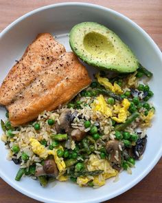 a white plate topped with rice, peas and salmon next to an avocado