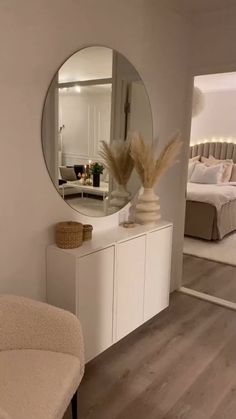 there is a mirror on the wall above a dresser in this living room with white furniture and wood flooring