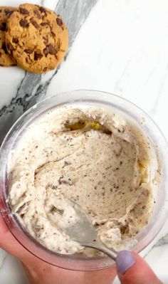 a hand holding a bowl of ice cream next to cookies