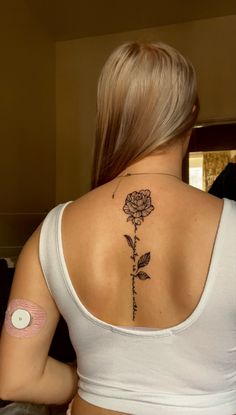 a woman with a rose tattoo on her upper back shoulder and behind her is a white tank top