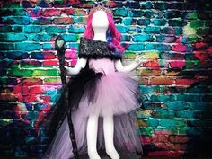 a doll dressed up as a princess holding a wand in front of a brick wall