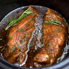 two pieces of meat in a slow cooker with herbs on the top and brown gravy