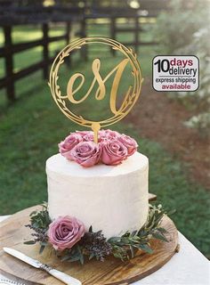 a white cake with pink flowers on top and a gold monogrammed name sign