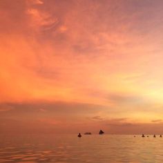 several boats floating in the ocean at sunset or dawn with pink and orange clouds above them