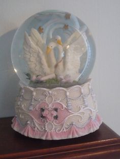 a snow globe with two white swans in it on top of a wooden table next to a wall