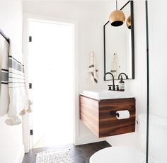 a white toilet sitting next to a bathroom sink under a mirror on top of a wooden cabinet