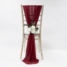 a white chair with a red sash and flowers on the armrest, sitting in front of a white backdrop