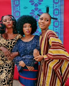 three women standing next to each other in front of a colorful wall