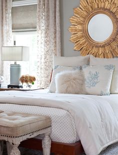 a white bed with pillows and blankets in a bedroom next to a large sun mirror