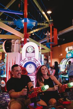 a man and woman sitting on the ground in front of an amusement park ride at night