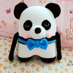 a stuffed panda bear with a blue bow tie sitting on a bed next to a pink wall