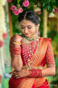 a woman in red and gold outfit holding her hands on her chest, with flowers behind her