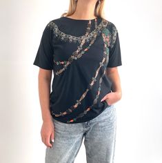 Gorgeous, glitzy black T-shirt with printed and embellished strings of beads. It has a straight shape with short sleeves and a boat neckline. The jersey fabric is lightweight and very soft. The design features lovely muted colours of bronze, beige, terracotta red and dark green and the beads are of all different types, including shiny gold, sparkly green and beautiful holographic flower beads, too. Perfect for the summer, paired with jeans or denim cut-offs. Made by Instyle. 65% polyester, 35% c Black Sequin Short Sleeve T-shirt, Embellished Graphic Tee With Crew Neck, Embellished Graphic Tee With Short Sleeves, Summer Black Embellished T-shirt, Black Embellished T-shirt For Party, Black Sequined T-shirt For Summer, Fitted Black Embellished T-shirt, Muted Colours, Cut Offs