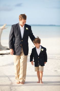 a man in a suit and tie holding the hand of a young boy wearing shorts