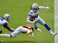 two football players are running for the ball and one is diving into the air to catch it