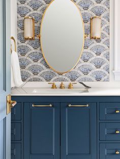 a bathroom vanity with blue cabinets and a gold framed mirror above it, along with an oval shaped mirror on the wall