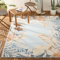 a blue and white rug with flowers on the floor next to a chair, potted plant