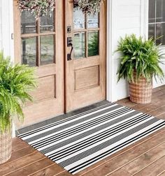 two potted plants sitting on the front porch next to a wooden door and rug