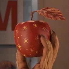 a person holding an apple in front of their face with leaves on top of it