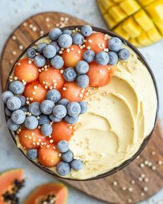 a cake with blueberries and oranges in it on a wooden platter next to sliced melons