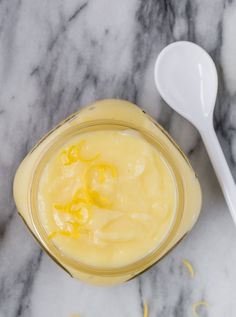 a spoon sitting on top of a jar filled with yellow liquid next to some lemon zest