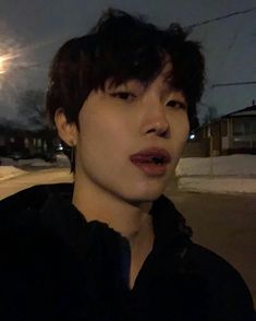 a young man standing in front of a street at night with the moon behind him